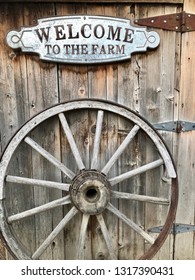 Welcome To The Farm Sign Above An Old Wagon Wheel In Front Of Barn Wood