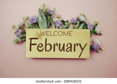 Welcome February Text On Wooden Board With Flowers Frame On Pink Background