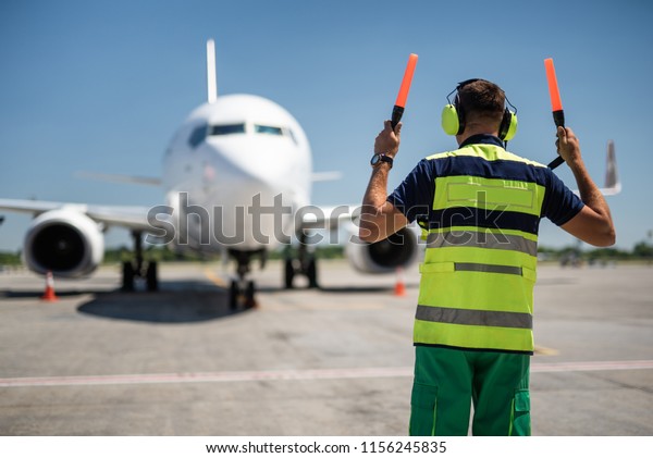 Welcome home. Back view of aviation marshaller\
directing aircraft\
landing