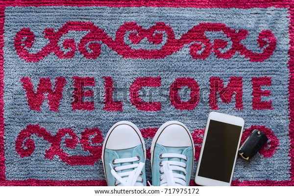 Welcome home carpet with shoes,smartphone and\
key of car on it,welcome\
concept.