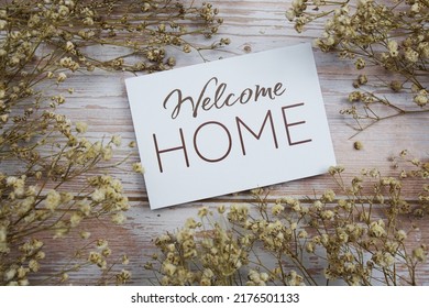 Welcome Home Text On Paper Card With Flower Decoration On Wooden Background