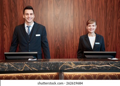 Welcome to the hotel. Male and female receptionists standing at the front desk with wooden background welcome guests with a smile 