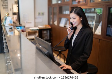 Welcome To The Hotel,Happy Young Asian Woman Hotel Receptionist Worker Smiling Standing,she Taking  Telephone Call At A Modern Luxury Reception Counter Waiting For Guests Getting Key Card In Hotel   