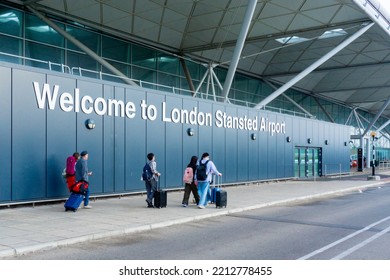 Welcome To London Stansted Airport Sign With A Group Of Travellers Walking Towards Departures. 