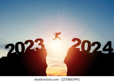 Welcome merry Christmas and happy new year in 2024,Silhouette Man jumping from 2023cliff to 2024 cliff with cloud sky and sunlight.