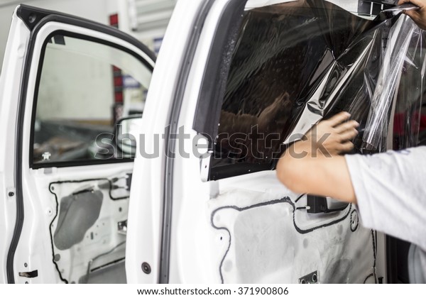 Welcome to our car service station. Closeup image\
of a car mechanic man attaching tinting film foil to car window in\
specialized service\
station