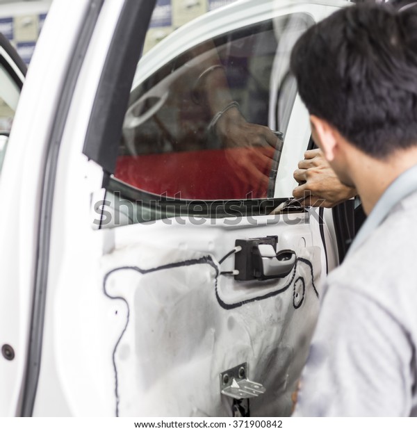 Welcome to our car service station. Closeup image\
of a car mechanic man attaching tinting film foil to car window in\
specialized service\
station