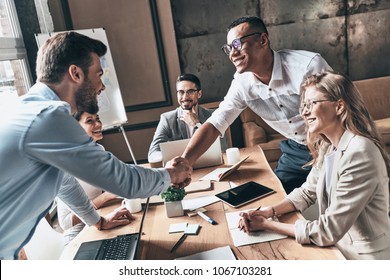 Welcome to our team! Top view of young modern men in smart casual wear shaking hands while working in the creative office - Shutterstock ID 1067103281