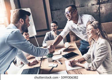 Welcome to our team! Top view of young modern men in smart casual wear shaking hands while working in the creative office - Shutterstock ID 1099306382