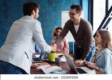 Welcome to our team! Young modern men in smart casual wear shaking hands while working in the creative office - Shutterstock ID 1323093350