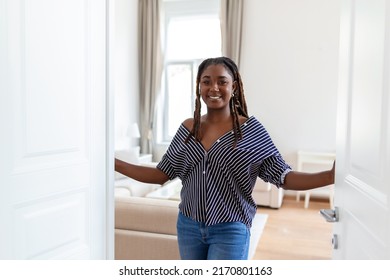 Welcome. Portrait of cheerful African woman inviting visitor to enter his home, happy young woman standing in doorway of modern apartment showing living room with hand - Powered by Shutterstock
