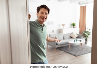 Welcome. Portrait of cheerful man inviting visitor to enter his home, happy young guy standing in doorway of modern apartment, millennial male holding door looking out showing living room with hand