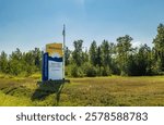 Welcome sign for British Columbia featuring provincial logo with sunrise over mountains, positioned in grassy field with evergreen forest background