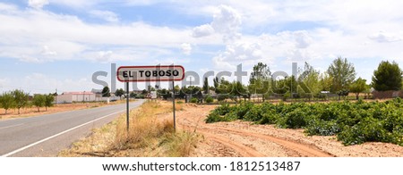 Welcome sign to El Toboso next to the road and vineyards.