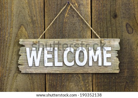 Welcome sign hanging by rope on rustic antique wood door; aged wooden  background