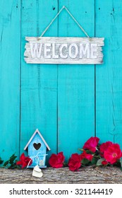 Welcome Sign Hanging On Antique Teal Blue Rustic Wood Background By Red Flowers And Birdhouse With Hearts On Log Border