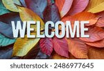 A welcome sign made of white letters on a background of colorful autumn leaves in various shades of red, orange, yellow, and green.