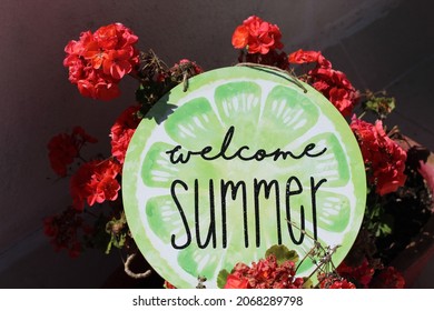 Welcome Summer Sign Hanging From Red Flowers. 