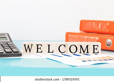 WELCOME Text On Wooden Building Blocks On Top Of Office Desk. Business Finance Meeting Or Workshop Presentation And Education Concept. Calculator And Binders. Onboarding Or Induction. Copy Space