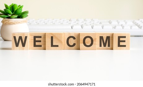 welcome word made with wooden blocks. front view concepts, green plant in a flower vase and white keyboard on background