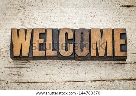 welcome word in vintage letterpress wood type on a grunge painted barn wood background