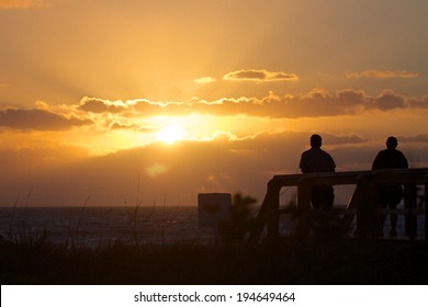 Welcoming A New Day 
Picture Of The Silhouette Of A Two Seniors On A Florida Boardwalk Watching The Sunrise Over The Ocean.