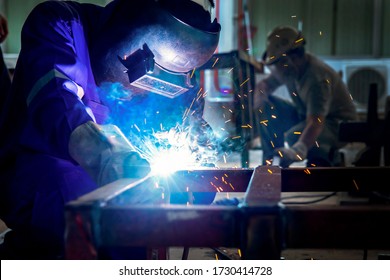Welder is assembling the workpiece by process shielded metal arc welding (SMAW). Welder in blue uniform, safety shoes, leather gloves, welding mask. He is sitting and welding. - Powered by Shutterstock - Get 15% off with code: PIKWIZARD15