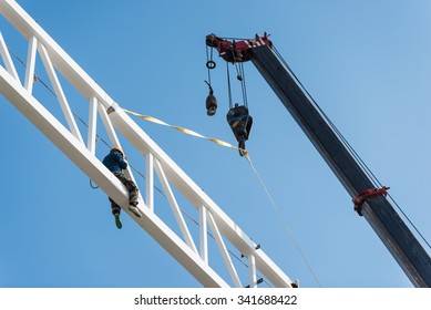 Welder climbing high on the steel structure on height and placing truss lifted by crane for installation work