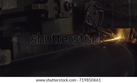 Welder complete with personal protective equipment is perform pipe welding in dark area using Automatic Welding System. Welding sparks spreading everywhere. Automat welding pipe production