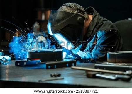 Welder creating a bright arc while joining metal pieces in a dark workshop, surrounded by tools and equipment.