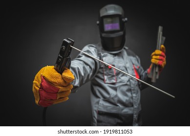 A welder in a helmet with a welding terminals in hand on a black background.