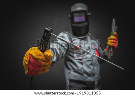 A welder in a helmet with a welding terminals in hand on a black background.