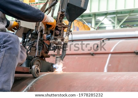 Welder operator is welding to pipe with submerged arc welding (SAW) method in the workshop. The process requires a continuously fed consumable solid or tubular (metal cored) electrode.