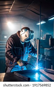 The welder performs welding task at his workplace in the factory, while the sparks "fly" around, he wears a protective helmet.