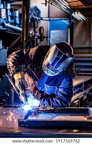 The welder performs welding task at his workplace in the factory, while the sparks 