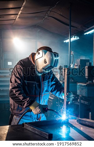 The welder performs welding task at his workplace in the factory, while the sparks "fly" around, he wears a protective helmet.