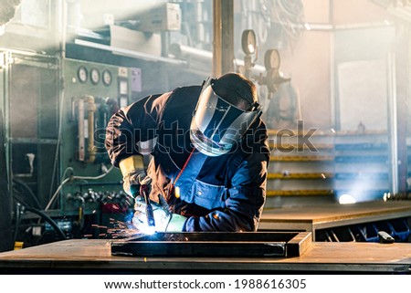 The welder performs welding task at his workplace in the factory, while the sparks 