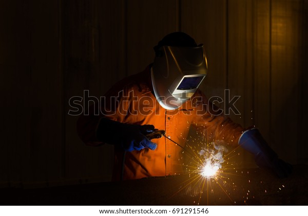 Welder with personal protective\
equipment and protective mask welding steel pipe in\
factory.