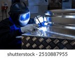 Welder with protective gear welding a metal structure in a workshop, focusing on the bright welding light and precision work.