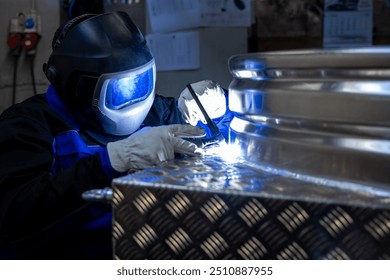 Welder with protective gear welding a metal structure in a workshop, focusing on the bright welding light and precision work. - Powered by Shutterstock