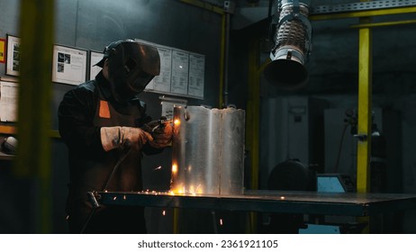 Welder in protective helmet, special apron and gloves. Male is soldering metal. Man at workplace in workshop with equipment. Variety of manufacturing professions. Dangerous type of activity. - Powered by Shutterstock