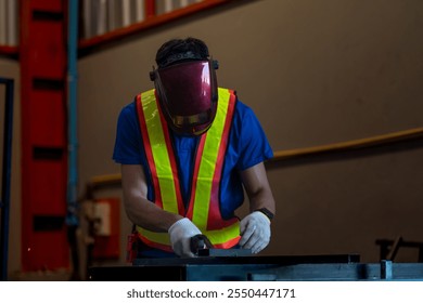 A welder in protective mask and reflective vest operates a welding torch, producing bright sparks in an industrial setting. He wears gloves and a blue shirt, focusing on metalwork with sparks flying. - Powered by Shutterstock