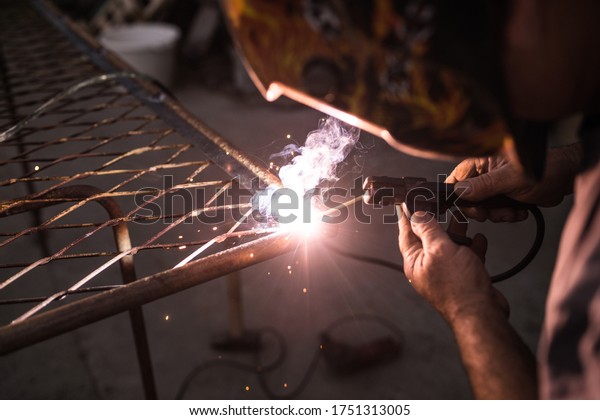 welder with protective mask welding\
steel structures and bright sparks in construction\
industry