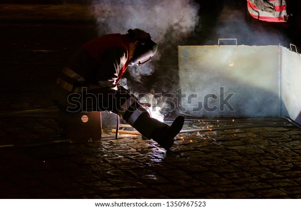 Welder repairing rail track on a cobblestone\
pavement by night