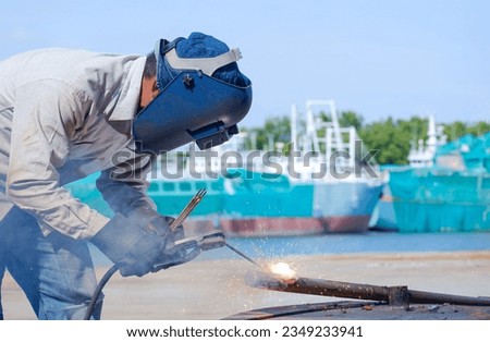 Welder with safety equipment using Arc Welding machine to welding galvanized steel pipe in Shipyard area at Harbor