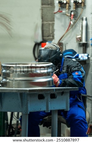 A welder seated at a workbench, welding a large metal ring, demonstrating precision and attention to detail in the workshop.