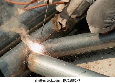 The Welder Is Sitting On The Steel Roof Frame And Is Welding.
