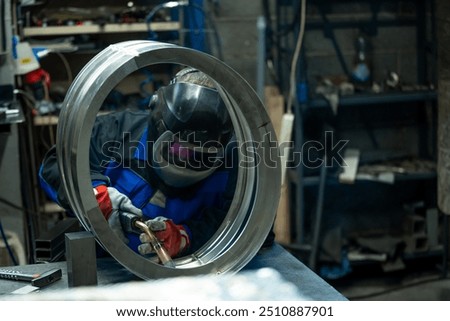Welder skillfully working on a large metal ring, carefully welding joints in a well-equipped workshop.