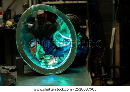 Welder skillfully working on a large metal ring, carefully welding joints in a well-equipped workshop.