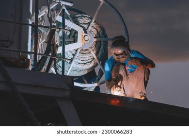 Welder using arc Welding machine to Repairing stern metal floor on deck of fishing boat in Shipyard area at Night